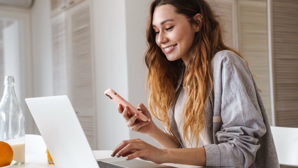 Mitarbeiterin plant den Dienstplan am Laptop und prüft ihn parallel auf dem Smartphone